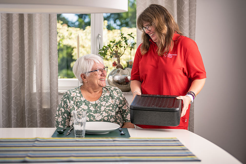 BRK Mitarbeiterin übergibt warmes Mittagessen vom Menüservice an Seniorin im Landkreis Günzburg